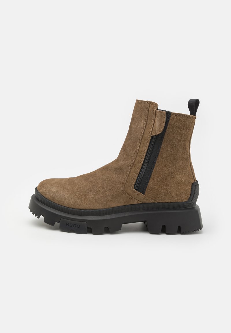 Brown suede ankle boot with a black side zipper, rugged black sole, and a tab at the back for easy wear. Elastic accents on the sides.