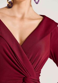 Burgunderrotes Wickelkleid mit tiefem V-Ausschnitt und drapierten Ärmeln, mit gerafftem Detail an der Taille und glattem, leichtem Stoff.