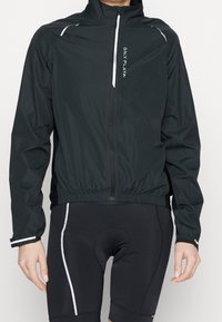 Chaqueta ligera negra con cremallera frontal, dobladillo elástico, detalles reflectantes y logo en el pecho. Mangas cortas y textura suave.