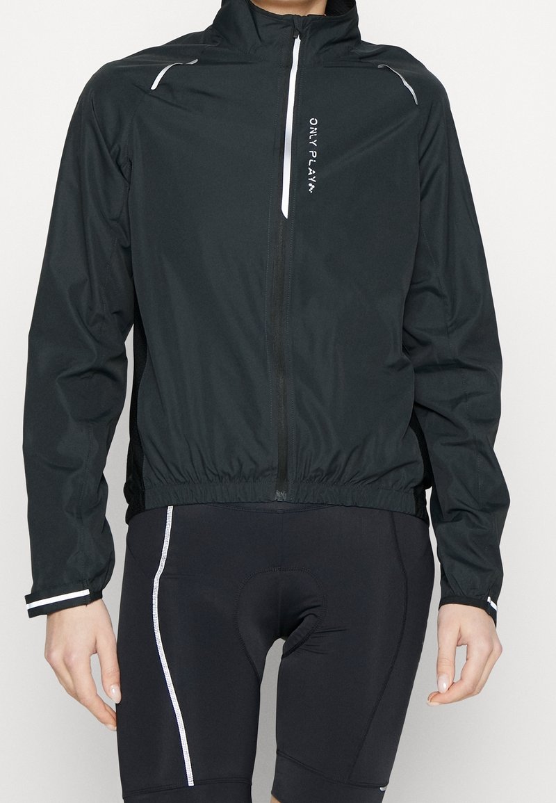 Chaqueta ligera negra con cremallera frontal, dobladillo elástico, detalles reflectantes y logo en el pecho. Mangas cortas y textura suave.