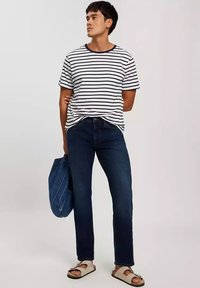 Pasiasta koszulka z krótkim rękawem w kolorze białym i granatowym, w zestawieniu z ciemnoniebieskimi dżinsami. Na nogach jasnobeżowe sandały, trzymając niebieską torbę typu tote z dżinsu.