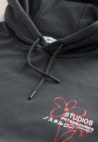 Felpa con cappuccio di colore grigio scuro, dotata di coulisse, grafica frontale con un fiore rosso e testo, e tessuto morbido e liscio.