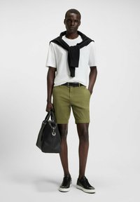 Olive green shorts, white t-shirt, black sweater tied around the neck, black belt, black leather bag, black sneakers with white soles.