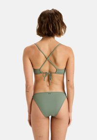 Grønt bikini-sett med knyt bak og kryssede stropper, med et enkelt design, glatt tekstur og minimalt med tilbehør på bunnene.