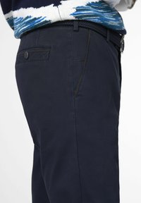 Navy trousers with a smooth texture, featuring a side pocket and visible stitching accents. Paired with a patterned, multi-colored sweater.