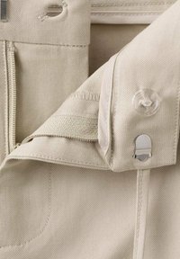 Béžové kalhoty s texturovanou látkou. Mají boční zip, zapínání na knoflík a měkký pas s klopou a háčkem.