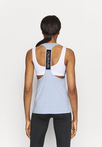Débardeur de sport bleu clair sans manches avec une couche intérieure blanche, un design dos découpé, et un détail étiquette de marque "CALVIN KLEIN" en noir.