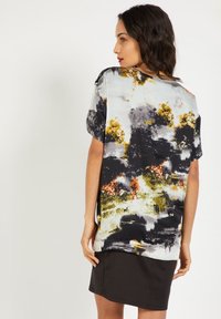 Blusa de manga corta y corte holgado en una tela suave y ligera, que presenta un estampado abstracto en negro, blanco y dorado.