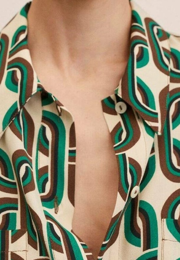 Chemise à manches courtes avec une base crème, présentant un motif abstrait audacieux en bleu sarcelle et marron. Comprend un col cranté et des détails à boutons.
