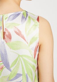 Top bez rękawów z teksturowanej tkaniny, ozdobiony dużymi zielonymi, fioletowymi i czerwonymi wzorami liści tropikalnych, widoczny z tyłu i z ramienia.