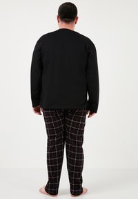Sort langærmet top med rund hals, parret med sorte og røde ternede pyjamasbukser. Bukserne har en lige benudskæring og ingen synlige lommer.