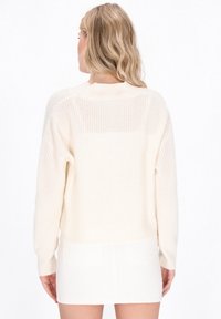 Maglione leggero di colore crema, con una vestibilità rilassata, texture a coste e maniche lunghe, caratterizzato da una schiena aperta e spalle basse.