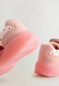 Chaussures de sport roses avec une semelle en caoutchouc texturé, présentant un dessus lisse et de petits motifs en forme de cœur. Le design est moderne et léger.