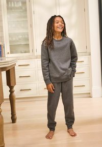 Ensemble en coton gris comprenant un sweatshirt et un pantalon de survêtement, avec un col rond, des manches longues et des poignets élastiques aux chevilles. Pas de motifs visibles ; texture lisse.