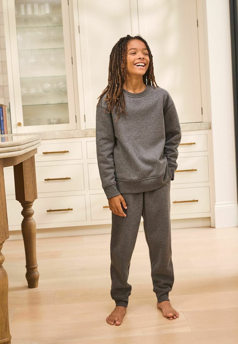 Ensemble en coton gris comprenant un sweatshirt et un pantalon de survêtement, avec un col rond, des manches longues et des poignets élastiques aux chevilles. Pas de motifs visibles ; texture lisse.