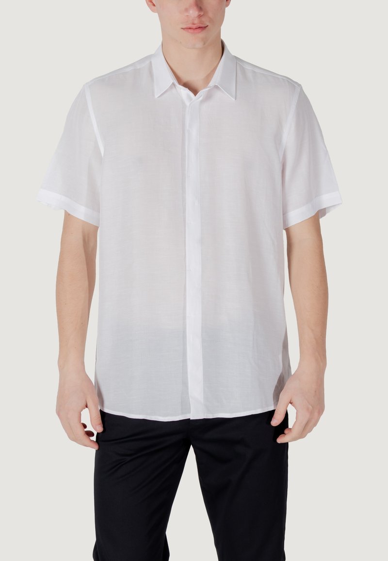Camisa blanca de manga corta y con botones, hecha de un tejido ligero con una textura suave y un cuello clásico. Diseño sencillo, sin patrones.