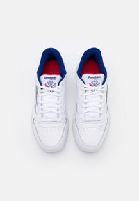 Pair of white Reebok Classic sneakers with blue inner lining and red insoles, viewed from above on a white background.