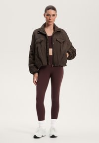 Brun puffjacka med voluminösa ärmar och fickor fram, som bärs med vinröda leggings och vita sneakers med svarta accenter.