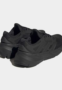 Black athletic shoes with a mesh upper, thick cushioned sole, and prominent logo details. Features a textured finish and rounded design.