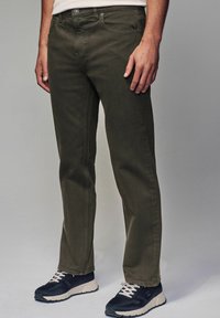 Donkergroene katoenen broek met een rechte pasvorm, vijf-pocket ontwerp en zichtbare stiksels, gecombineerd met zwarte sneakers met witte veters.