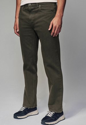 Dark green cotton pants with a straight fit, five-pocket design, and visible stitching, paired with black sneakers featuring white laces.