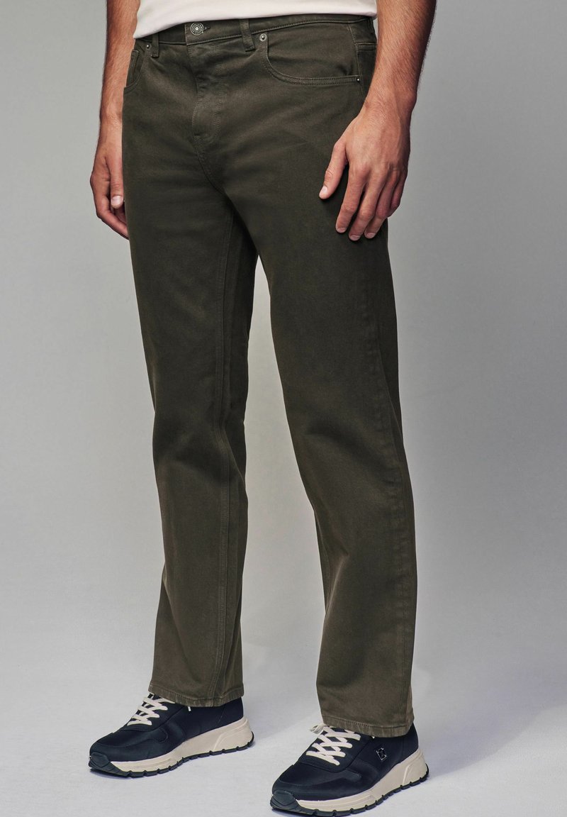 Donkergroene katoenen broek met een rechte pasvorm, vijf-pocket ontwerp en zichtbare stiksels, gecombineerd met zwarte sneakers met witte veters.