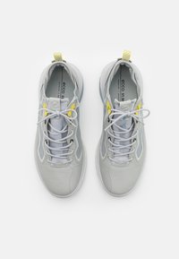 Light gray athletic shoes with mesh and smooth textures. Features include yellow accents, round laces, and a padded collar.