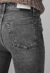 Jeans de mezclilla gris con un diseño ajustado, una cintura de altura media y un bolsillo trasero con costuras sutiles. La etiqueta dice "RE/DONE". Textura suave.