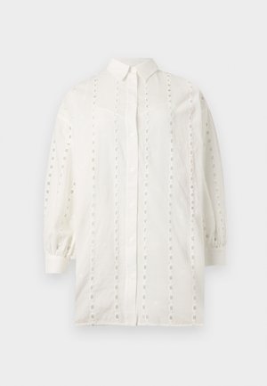 Bijela košulja dugih rukava s kopčanjem na gumbe, okomite pruge od čipke s otvorima, ovratnik i skupljene manžete na jednobojnoj pozadini.