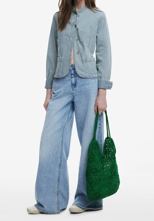 Veste en denim rayée bleue et blanche avec trois boutons, associée à un jean large délavé et un sac en crochet vert.