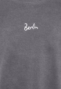 Grå sweatshirt med texturerad finish, med en vit broderad "Berlin"-text i en avslappnad stil. Standard rund halsringning.