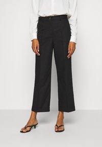 Zwarte wijde broek met een gladde textuur, met een knoopsluiting en een omgeslagen zoom. Gecombineerd met zwarte open teenvrouwen.