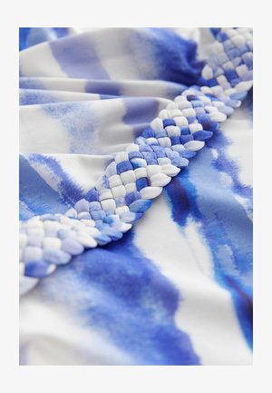 Blåt og hvidt mønstret stof med en flettet kant, der inkluderer sammenvævede teksturer, og som præsenterer en glat overflade og et akvarel-lignende design.