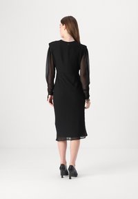Rochie neagră cu mâneci pufoase transparente, talie ajustată și tiv până la genunchi. Dispune de un închidere cu buton la spate. Textură de țesătură netedă.