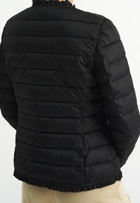 Černá polstrovaná bunda s horizontálním prošíváním, volánkovým výstřihem a olemovaným lemem. Hladká textura, přiléhavý střih a krátké rukávy.