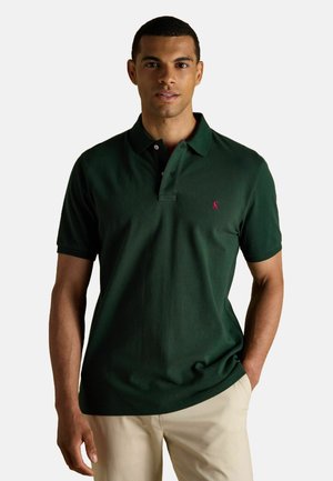Dunkelgrünes Poloshirt aus Baumwolle, mit einem Drei-Knopf-Verschluss, kurzen Ärmeln und einem kleinen pinken Logo auf der linken Brust.