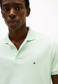 Lichtgroene poloshirt van katoen, met een knoopsluiting van drie knopen en een klein merklogo op de borst. Zachte textuur.