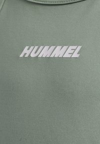 Grünes Sportshirt mit rundem Ausschnitt und weißem "HUMMEL"-Logo auf der Brust gedruckt. Das Material hat eine strukturierte, atmungsaktive Optik.