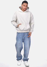 Hellbeige Hoodie mit einer Fronttasche, im entspannten Schnitt. Kombiniert mit lockeren hellblauen Jeans und weißen Sneakers.