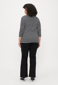 Czarna i biała w paski bluzka z długim rękawem o okrągłym dekolcie, połączona z czarnymi spodniami w kant i szpilkami, widok z tyłu.