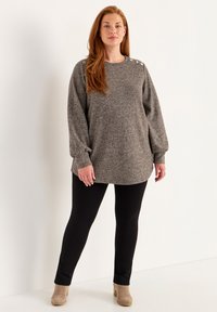 Grijze gebreide tuniek met ronde hals, lange mouwen en knopenaccenten op de schouder, gecombineerd met zwarte legging en beige enkellaarsjes.