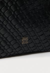 Μαύρη υφαντή δερμάτινη τσάντα με χρυσαφί διακοσμητικό λογότυπο. Υφή με χαρακτηριστικά ορθογώνια σχέδια σε όλη την επιφάνεια.