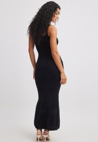 Black, fitted knit maxi dress with a sleeveless design, textured fabric, and a flared hem. The model wears nude high heels.