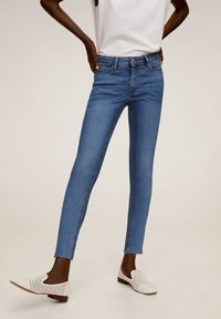 Lichtblauwe skinny jeans van denimstof, met een medium taille en rafelige enkelhemlijnen, gecombineerd met witte geperforeerde instapschoenen.