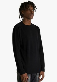 Maglione nero a maniche lunghe in tessuto morbido con scollo rotondo e polsini a coste, dal taglio ampio e rilassato.