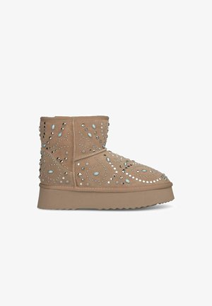 Tan ankle boots with a textured surface, embellished with silver and blue studs in a swirling pattern, featuring a thick sole and rounded toe.