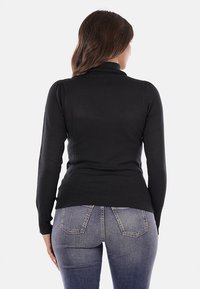Maglione nero a maniche lunghe con colletto alto, design aderente e orlo a coste, abbinato a jeans blu con tasche posteriori classiche.