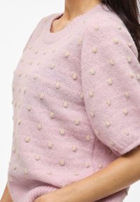 Suéter de punto rosa claro con escote redondo y mangas cortas, adornado con puntos beige texturizados en toda la tela.