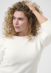 Cream-colored knit sweater with a round neckline and three-quarter sleeves, featuring a soft texture and subtle ribbed details.
