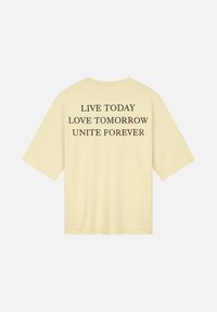 Gele katoenen t-shirt met een losse pasvorm, voorzien van zwarte tekst op de rug: "LEEF VANDAAG, HOU VAN MORGEN, VERENIG VOREND." Korte mouwen, ronde halslijn.